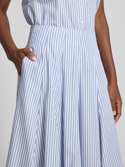 Vrouwenmodel draagt Midirok met zij-steekzakken van Gant in blauw-wit gestreept puur katoen, A-lijn, detailopname taille en rok.