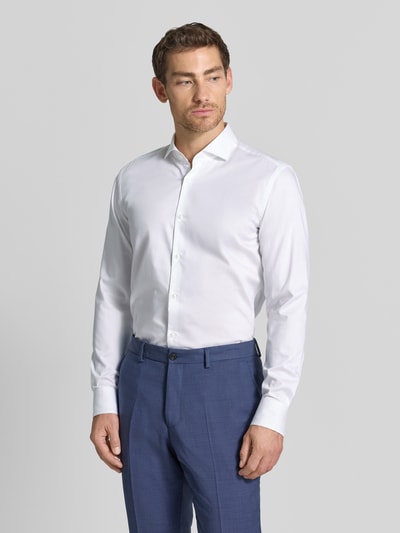 Männermodel trägt weißes Slim Fit Businesshemd aus reiner Baumwolle Modell 'Kason' von HUGO zu blauer Hose, Ganzkörperansicht von vorne.
