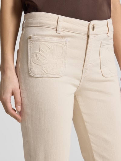 Kobieta prezentuje Flared Fit Jeans mit aufgesetzten Taschen Modell 'Ashley' od MOS MOSH, mieszanka bawełny, nakładane kieszenie, kolor jasny, zapięcie na guzik i zamek błyskawiczny, szerokość w rozmiarze 27: 39 cm, długość wewnętrzna nogawki w rozmiarze 27: 76 cm, zbliżenie na górną część nóg.