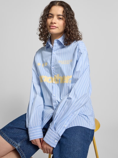 Frauenmodel trägt Relaxed Fit Bluse mit Label-Print von ANOTHER COTTON LAB aus reiner Baumwolle, blau mit weißen Streifen, Hemdblusenkragen, Knopfleiste, Vorderansicht, Nahaufnahme Oberkörper.