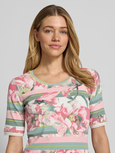 Modelka kobieca nosi T-Shirt mit floralem Allover-Print von Betty Barclay z mieszanki bawełny, dopasowany krój, okrągły dekolt, rękaw o dł. 1/2, różowe i zielone pasy z kwiatowym nadrukiem na całej powierzchni, długość tyłu w rozmiarze 36: 58 cm, zbliżenie górnej części ciała z przodu.