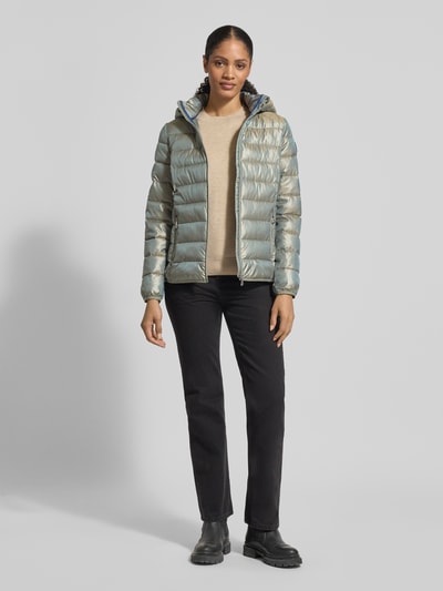 Modelka kobieca ma na sobie Jacke mit Kapuze od NAUTGÅRD w luźnym kroju, kolor metaliczny, z kapturem, sznurkiem, zakrytym zamkiem, detalem z logo, paskami przy rękawach; długość tyłu w rozmiarze M: 90 cm, szerokość ramion w rozmiarze M: 45 cm, szerokość w klatce piersiowej w rozmiarze M: 56 cm, długość rękawa w rozmiarze M: 60 cm; pełny widok z przodu