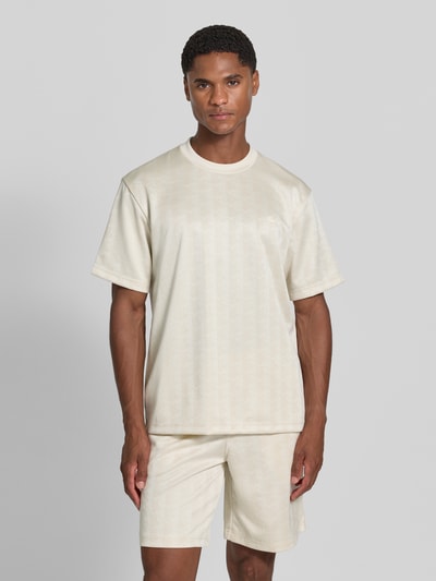 Männermodel trägt Regular Fit T-Shirt mit Allover-Muster von Lacoste in Creme mit feiner Struktur, Herren T-Shirt, Ganzkörperansicht von vorne.