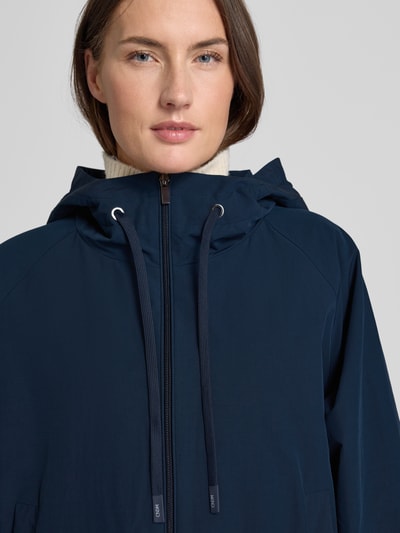 Frauenmodel trägt Relaxed Fit Regenjacke mit Baumwoll-Anteil Modell 'ROMANA' von Weekend Max Mara in Dunkelblau, Nahaufnahme Oberkörper, unifarbene Optik, Kapuze mit Tunnelzug, wasserabweisendes Material, Logo-Patch, seitliche Taschen