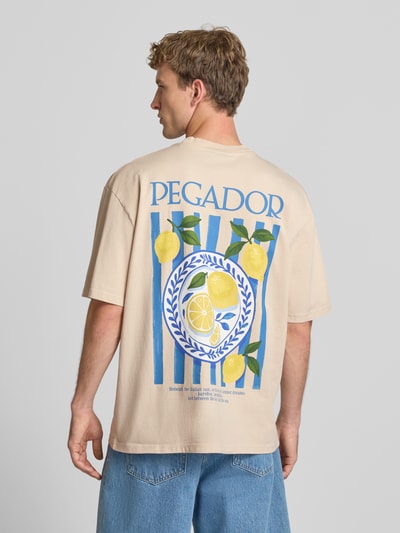 Männermodel trägt Oversized T-Shirt mit Backprint und Rundhalsausschnitt von PEGADOR in Beige mit buntem Zitronen-Print aus reiner Baumwolle, Ganzkörperansicht Rückansicht.