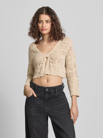 Modelka nosi Cropped Strickjacke aus Baumwoll-Mix Modell 'BEACH LIFE' od Only, kremowy, luźny krój, ażurowy wzór, długi rękaw, bawełniany mix, widok całej sylwetki z przodu.