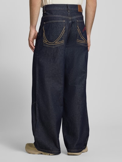 Männermodel trägt Wide Fit Jeans mit Logo-Stitching von KARL KANI in Dunkelblau, 5-Pocket-Design, reine Baumwolle, Ganzkörperansicht Rückansicht.
