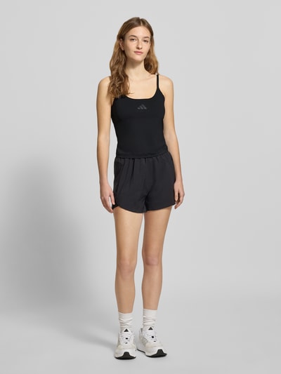 Frauenmodel trägt Tanktop mit Label-Print von adidas Sportswear in Schwarz, Slim Fit, Material-Mix mit Stretch-Anteil, Ganzkörperansicht von vorne.