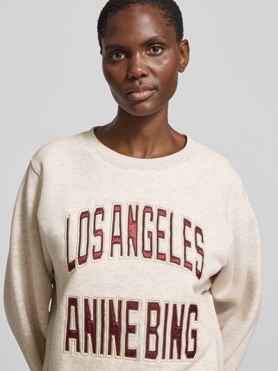 Frauenmodel trägt Oversized Sweatshirt aus Baumwoll-Mix von Anine Bing in Beige mit Rundhalsausschnitt und Label-Stitching, Nahaufnahme Oberkörper.