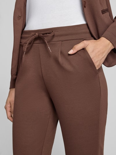 Frauenmodel trägt Slim Fit Hose mit Viskose-Anteil Modell 'KATE' von ICHI, braun, strukturierte Oberfläche, Nahaufnahme Oberkörper, Damen Hose elastischer Bund mit Tunnelzug, verkürzte Passform, KI-modifiziertes Bild.
