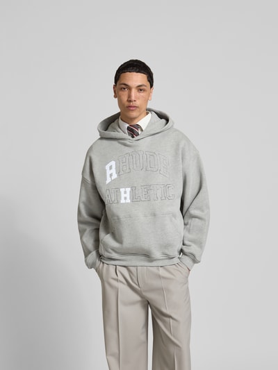 Männermodel trägt Oversized Hoodie mit Logo-Print von RHUDE, grau, Baumwoll-Mix, elastische Abschlüsse, Känguru-Tasche, Ganzkörperansicht von vorne.