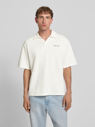 Männermodel trägt Regular Fit Poloshirt mit Logo Modell 'Eddie' von Redefined Rebel, Baumwoll-Mix, V-Ausschnitt, weiße Farbe, Ganzkörperansicht von vorne.