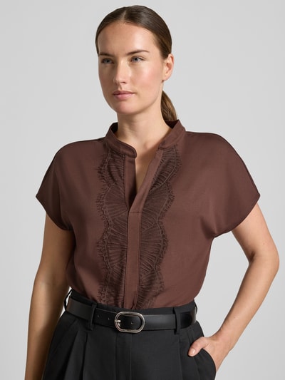 Frauenmodel trägt Regular Fit Bluse aus Baumwoll-Mix mit Spitzenbesatz von Marc Cain, braun, Serafino-Ausschnitt, Kurzarm, Nahaufnahme Oberkörper. Rückenlänge bei Größe 36: 57 cm, elastischer Stoff, schlichte Struktur.