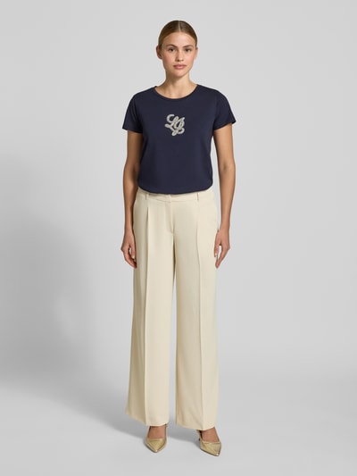 Frauenmodel trägt T-Shirt mit Rundhalsausschnitt und Strasssteinbesatz von LIU JO SPORT in Dunkelblau, reine Baumwolle, gerader Schnitt, Logo-Detail, Ganzkörperansicht von vorne.