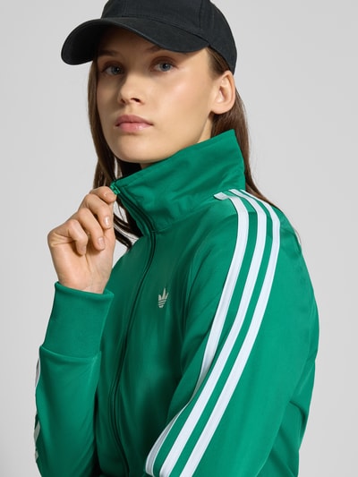 Kobiece model prezentuje Trainingsjacke mit Label-Stitching od adidas Originals, zielony kolor, krój regular fit, stójka, zamek, przednie kieszenie na zamek, widok z przodu zbliżenie na górną część ciała.