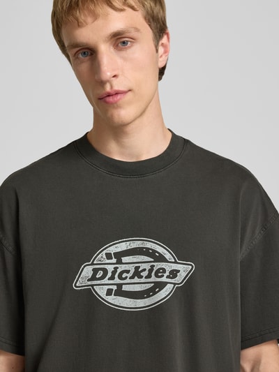 Männermodel trägt schwarzes T-Shirt mit weißem Logo-Print, reine Baumwolle, Relaxed Fit, PLAINVILLE von Dickies, Nahaufnahme Oberkörper.