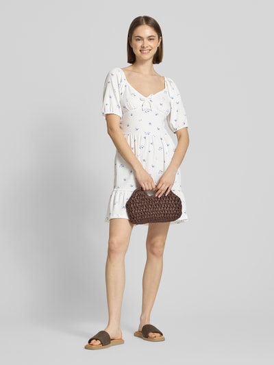 Frauenmodel trägt Minikleid mit Puffärmeln Modell 'HILLARY' von Only, Optik:Allover-Muster, tailliert, Mini-Länge, Karree-Ausschnitt, florales Muster, Schleife, Materialverarbeitung: Crêpe, helle Farben, Ganzkörperansicht von vorne.