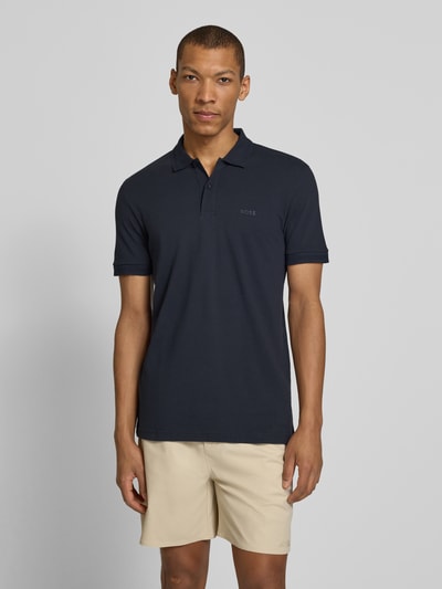 Mężczyzna nosi koszulkę polo Regular Fit Poloshirt aus reiner Baumwolle Modell 'PIO 1' von BOSS Green, efekt: jednolity kolor, krój regular fit, wytłaczane logo, kołnierzyk polo, dekolt w serek, krótką listwę guzikową, krótki rękaw, prążkowane zakończenie rękawów, wykończenie materiału: bawełna, ganzkörperansicht von vorne.