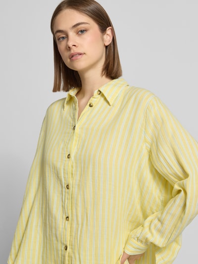 Frauenmodel trägt Loose Fit Hemdbluse aus reiner Baumwolle Modell 'THYRA' von Only, Optik:Allover-Muster, Muster: Gestreift, Hemdkragen, einreihige Knopfleiste, Kurzarm, Gelb mit weißen Streifen, Struktur wirkt leicht und weich, Nahaufnahme Oberkörper.
