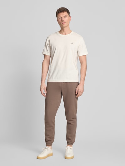 Męski model nosi Sweatpants mit Eingrifftaschen od GAP, mieszanka bawełny, krój regular fit, pas elastyczny, logo, długość wewnętrzna nogawki 72 cm, wpuszczane kieszenie, widok całej sylwetki z przodu.