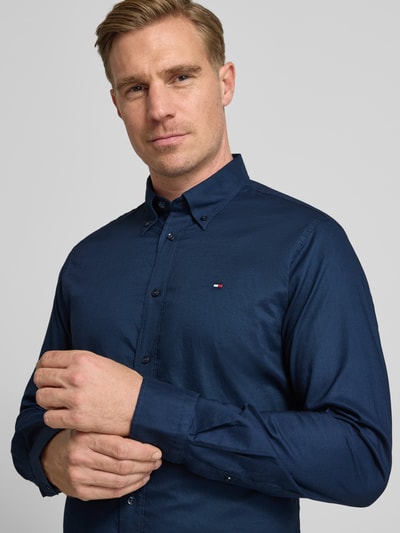Męski model nosi Regular Fit Businesshemd aus reiner Baumwolle von Tommy Hilfiger, ciemnoniebieska, jednolita tkanina, długi rękaw, zbliżenie na górną część ciała.