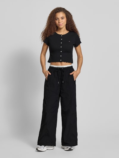 Kobiece modelka nosi Slim Fit T-Shirt aus Baumwoll-Mix von Tommy Jeans, czarny, gładki, logo, krótki rękaw, frill, ripp, widok z przodu cała sylwetka.