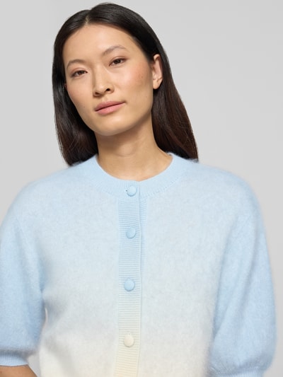 Frauenmodel trägt Strickjacke aus Kaschmir-Baumwoll-Mix mit 1/2-Arm von HERZENS in Hellblau-Weiß, Rundhalsausschnitt, Knopfleiste, Puffärmel, Regular-Fit, weiche und glatte Textur, Rückenlänge 56 cm, Ärmellänge 26 cm, Nahaufnahme Oberkörper.
