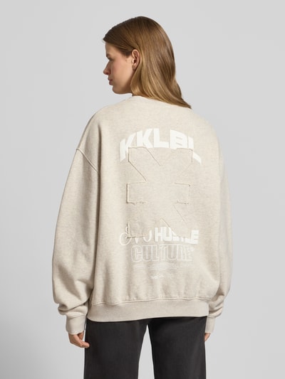Frauenmodel trägt Sweatshirt mit rückseitigem Statement-Print Modell 'No Hustle' von Karo Kauer aus Reine Baumwolle, Oversized-Fit, beige, Logo-Print, gerippte Abschlüsse, Rundhalsausschnitt, Ganzkörperansicht Rückansicht.