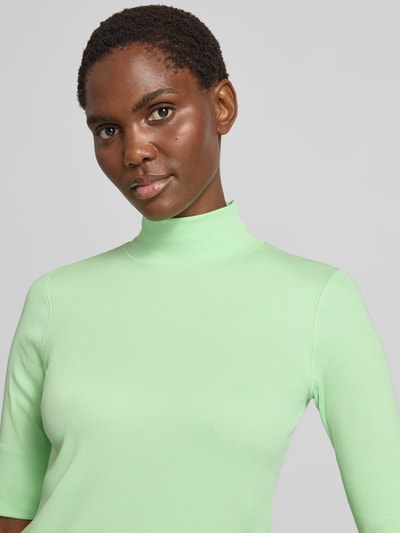 Frauenmodel trägt Slim Fit T-Shirt aus Baumwoll-Mix mit Stehkragen von Marc Cain in Hellgrün, glatte Textur, Nahaufnahme Oberkörper.