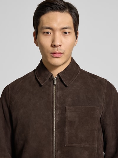 Männermodel trägt Lederjacke mit Reißverschluss Modell 'JERSON' von Drykorn in Braun aus Echtleder mit Umlegekragen und Brusttasche, Nahaufnahme Oberkörper.