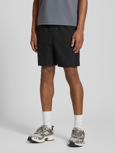 Männermodel trägt schwarze Relaxed Fit Shorts mit Logo-Patch von Lacoste, Herren Sportshorts, glatte Textur, Ganzkörperansicht von vorne.