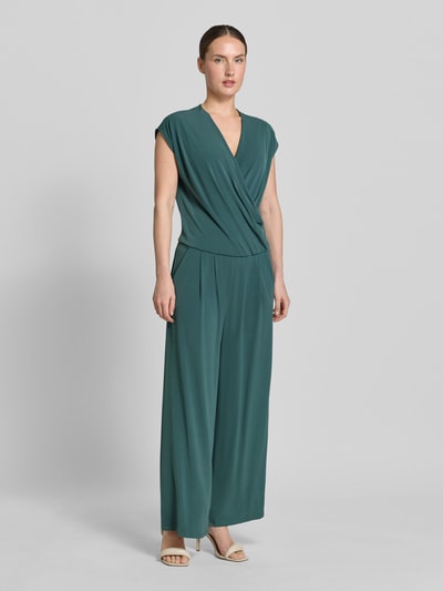 Modelka nosi Jumpsuit in Wickel-Optik mit V-Ausschnitt od ROBE LÉGÈRE w kolorze ciemnozielonym, materiał z domieszką stretchu, krój regular fit, dekolt w serek, długość tyłu w rozmiarze 36: 49 cm, szerokość w rozmiarze 36: 42 cm, długość całkowita w rozmiarze 36: 147 cm, długość nogawki wewnętrznej w rozmiarze 36: 63 cm, widok całej sylwetki z przodu.