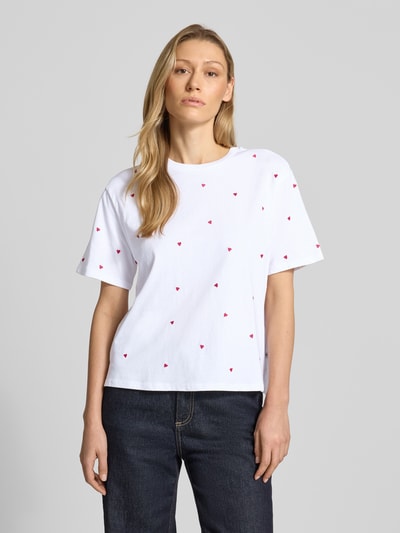Frauenmodel trägt Boxy Fit T-Shirt aus reiner Baumwolle von Tom Tailor Denim, weiß, unifarben, Allover-Herz-Stickerei, Rundhals, Kurzarm, mit Seitenschlitzen, Ganzkörperansicht von vorne.