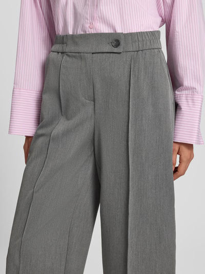 Vrouwenmodel draagt stoffen broek Model 'Cisilia' van someday., grijze kleur, Materiaalmix met viscose, steekzakken, knoop- en ritssluiting, persplooien, strookzak aan de achterkant, comfortband, barrel fit, Binnenbeenlengte maat 36: 64 cm, Bandwijdte maat 36: 38 cm, Nahaufnahme taille en bovenbenen.