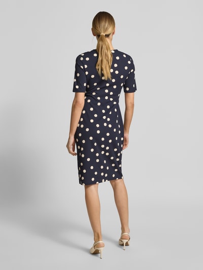 Vrouwenmodel draagt Tailliertes Midikleid in Wickeloptik van s.Oliver BLACK LABEL met donkerblauwe polkadots, midi, getailleerde fit, korte mouw, V-hals, O-ring detail. Volledige lichaamsaanzicht achteraan.