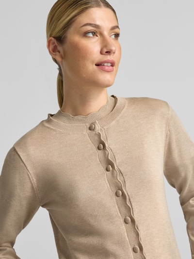 Frauenmodel trägt Strickjacke aus Viskose-Mix Modell 'MORLA' von b.young in Beige mit Knopfleiste, Nahaufnahme Oberkörper. Gerader Schnitt, elastische Ärmelabschlüsse mit Muschelsaum, Rückenlänge 55 cm, Ärmellänge 62 cm.