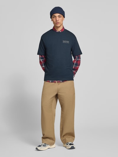 Männermodel trägt Relaxed Fit T-Shirt aus reiner Baumwolle von Marc O'Polo DENIM, dunkles Blau, kombiniert mit beigem Hose, Ganzkörperansicht von vorne.