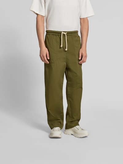 Männermodel trägt Balloon Fit Stoffhose aus Baumwolle von Officine Générale in Olivgrün mit elastischem Bund, Canvas-Struktur, Ganzkörperansicht von vorne.