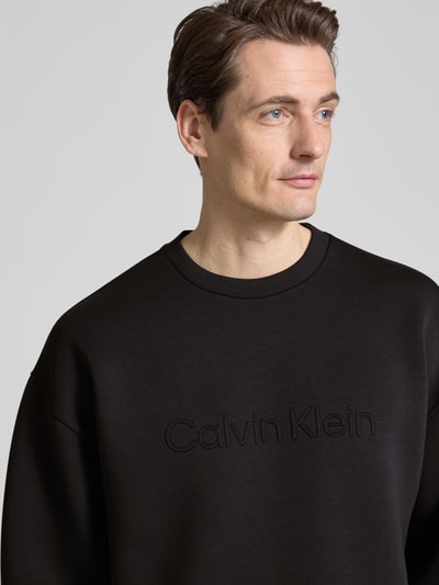 Męski model nosi Bluza 'Sweatshirt mit Rundhalsausschnitt und Logo' od CK Calvin Klein, mieszanka materiałów z dodatkiem wiskozy, krój regular fit, okrągły dekolt, logo, długość tyłu w rozmiarze M 61 cm, długość rękawów 59 cm, gładka faktura, kolor czarny, zbliżenie na górną część ciała