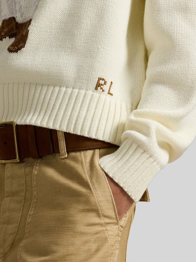 Kobiece modelka nosi Regular Fit Strickpullover mit Polo Bear od Polo Ralph Lauren, kremowy bawełniany sweter, dzianina, długi rękaw, gładki wzór, ściągacze, detal Polo Bear, krój regular fit, zbliżenie na dolną część tułowia.