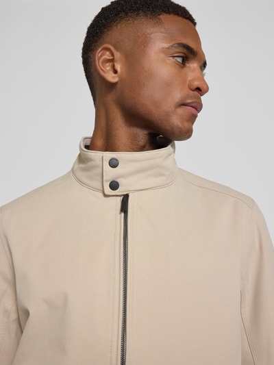 Männermodel trägt Regular Fit Blouson mit Stehkragen von Tom Tailor in Beige, unifarbenes Twill, Sicht auf Reißverschluss und Label Patch, Nahaufnahme Oberkörper.