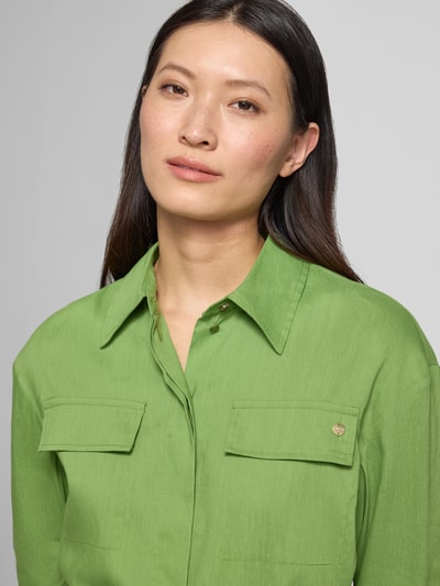 Frauenmodel trägt Bluse aus Leinen-Mix mit Brusttaschen von Marc Cain in grün, Tailliert, Umlegekragen, Nahaufnahme Oberkörper. Damen Bluse aus elastischem Leinen-Mix mit Viskose-Anteil, Brusttaschen, abnehmbarem Stoffband, Rückenlänge 69 cm, Ärmellänge 55 cm in Größe 36.