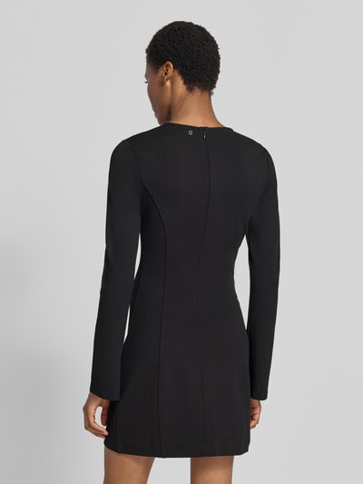 Vrouwenmodel draagt knielang zwart knielang jurk met stretch van Model 'CLAUDIE' van GUESS, elastische materiaalmix, getailleerde pasvorm, ronde hals, met lange mouwen, cut-outs met siersteentjes, ruglengte maat S 95 cm, borstwijdte 40 cm, mouwlengte 67 cm, geheel effen textuur, achteraanzicht op volledige lengte.