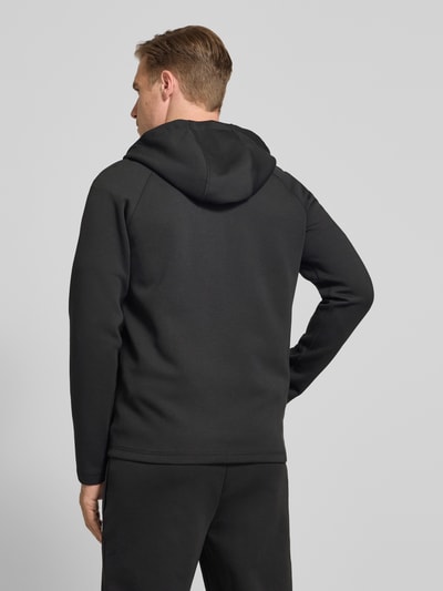 Männermodel trägt Regular Fit Sweatjacke mit Baumwoll-Anteil von Lacoste, efekt: jednolity kolor, krój regular fit, zamek błyskawiczny, naszywka z logo, kaptur z tunel, długi rękaw, wpuszczane kieszenie, wykończenie materiału scuba, mieszanka bawełny, Ganzkörperansicht Rückansicht.