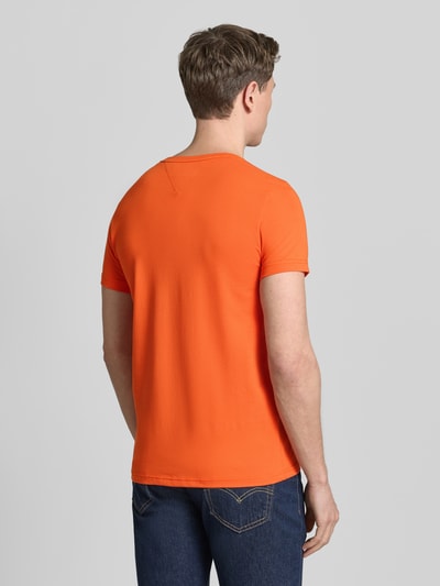 Męski model nosi Slim Fit T-Shirt aus Baumwoll-Mix von Tommy Hilfiger w jednolitym pomarańczowym kolorze, krój slim fit, logo, okrągły dekolt, krótkie rękawy, materiał elastyczny, bawełniany miks, całkowity widok z tyłu.