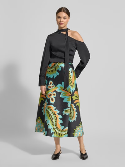 Frauenmodel trägt Midirock aus Satin im Allover-Look von HERZENS in Schwarz mit buntem Muster, A-Linie, Teilungsnähte, Reißverschluss, Ganzkörperansicht von vorne.