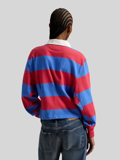 Frauenmodel trägt Regular Fit Poloshirt aus reiner Baumwolle von Polo Ralph Lauren, gestreift rot-blau, Polokragen, Ganzkörperansicht Rückansicht.