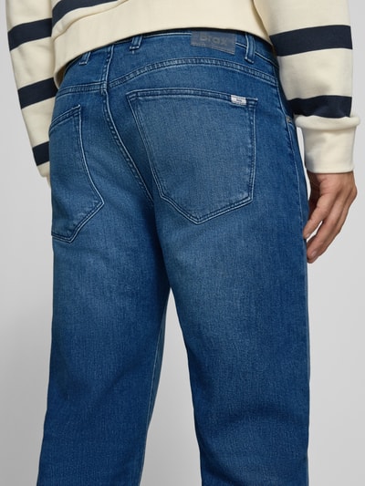 Männermodel trägt Relaxed Fit Jeans aus Baumwoll-Mix Modell 'Clint' von Brax, blaue Jeans, dezente Waschung, Herren Wide & Loose Fit Jeans, Ganzkörperansicht Rückansicht.