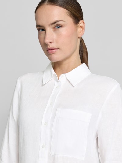 Frauenmodel trägt Leinenbluse mit Brusttasche Modell 'LINO' von Mango in Weiß, reines Leinen, Kentkragen, Knopfleiste, Loose-Fit, Nahaufnahme Oberkörper.