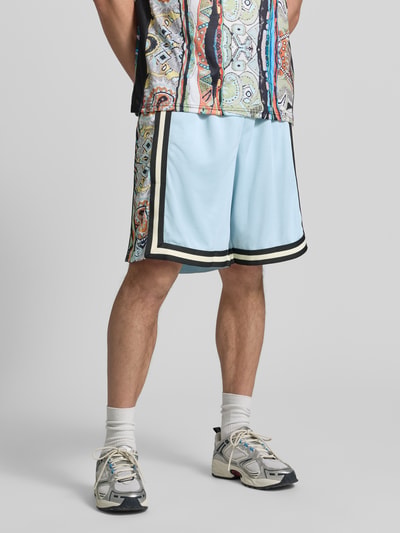 Mężczyzna nosi Shorts aus Mesh mit Kontraststreifen von COLUCCI w kolorze jasnoniebieskim z czarnymi paskami, prosty krój, elastyczny pas, szerokość w rozmiarze M: 37 cm, długość nogawki od kroku w rozmiarze M: 24 cm, tekstura siateczkowa, widok całej sylwetki z przodu.